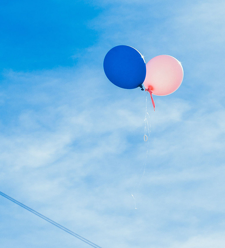 Friends celebrating a gender reveal with balloons and confetti
